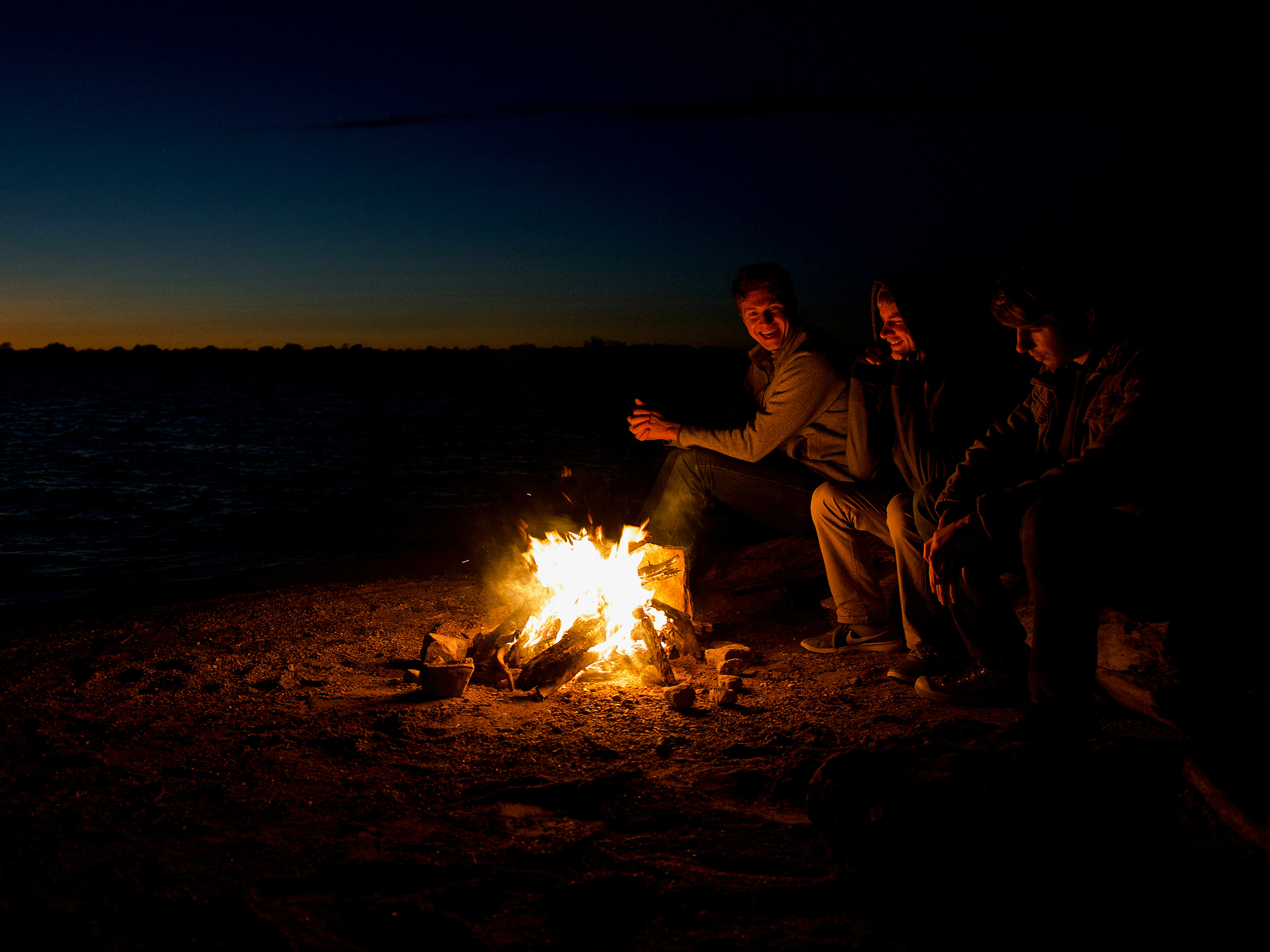 Friends around a lakeside campfire at dusk